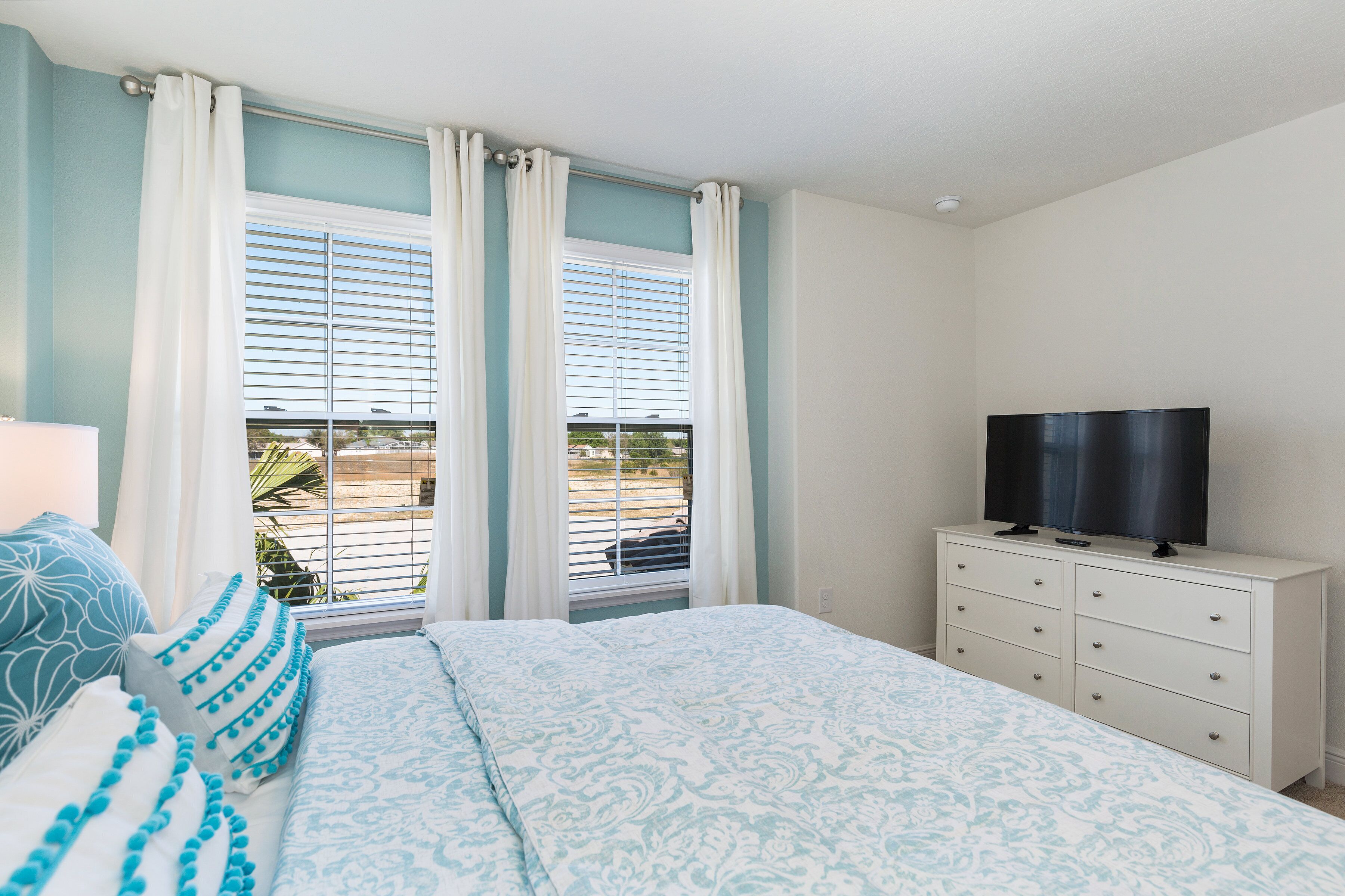 A bedroom with a bed, a dresser, a television, and a window with blinds.
