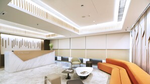 Un lobby moderno de hotel con una recepción, zonas de estar y un techo alto con iluminación empotrada.