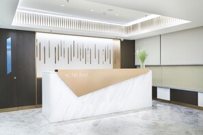 A modern hotel reception desk with a marble counter, a vertical light panel, and a potted plant. - Hotel Ease Access Wan Chai (Hong Kong)