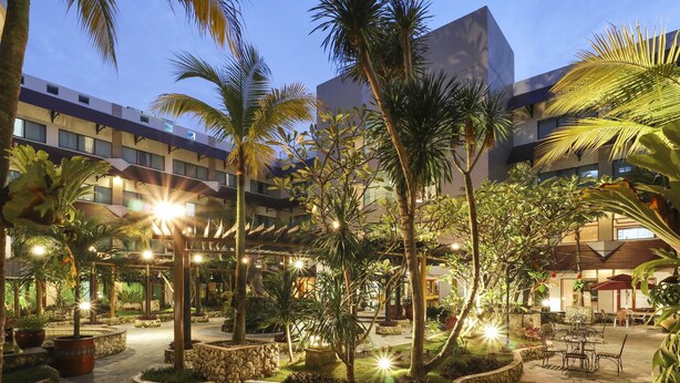 An outdoor courtyard with palm trees, stone planters, and outdoor seating. - AP Premier Batam (Batam)