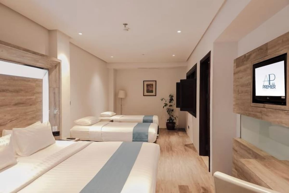 Habitación de hotel con dos camas, un televisor montado en la pared y una pared decorativa de madera.