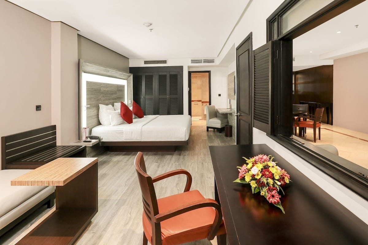 A modern hotel room with a bed, a desk, a chair, and a large window.