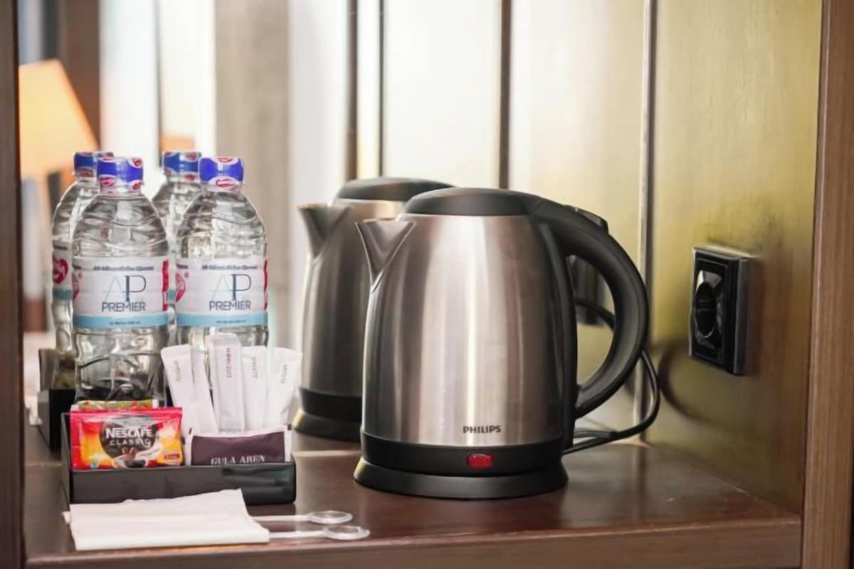 Habitación de hotel con minibar que contiene botellas de agua, una tetera y una caja de café Nescafe Classic.