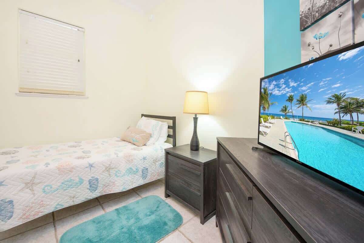 A bedroom with a bed, bedside table, lamp, TV, and a view of a swimming pool.