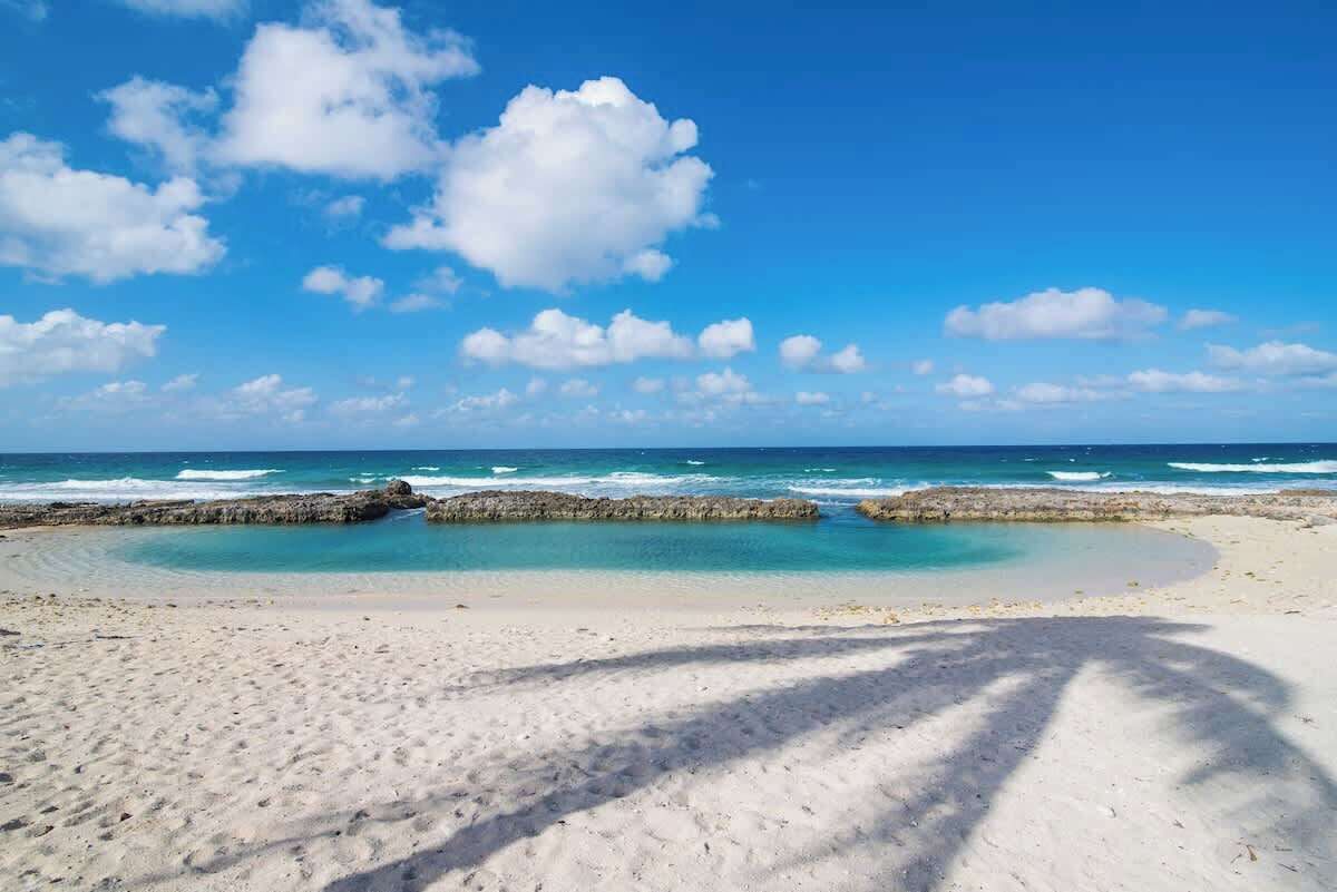 A beach with clear skies, calm sea, and rocky formations.