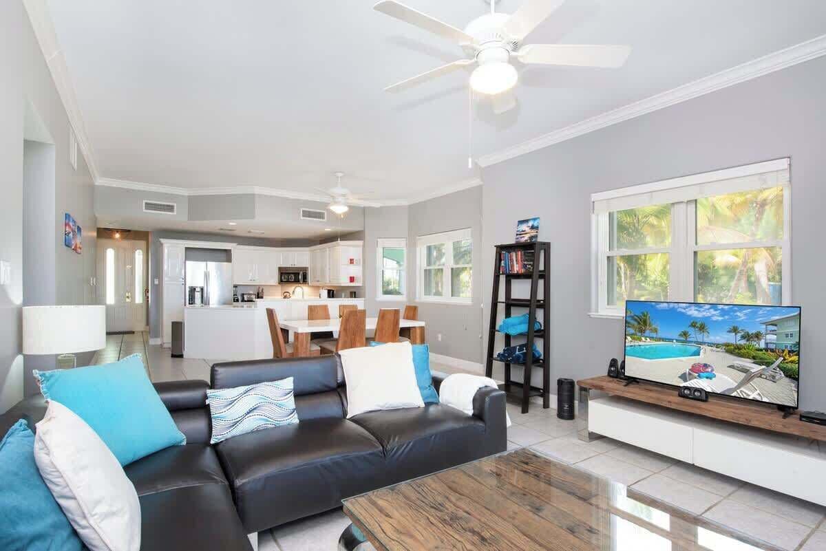 Una sala de estar moderna con sofá, mesa de centro y televisor, comunicada con una cocina y comedor.