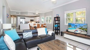 A modern living room with a sofa, coffee table, and TV, connected to a kitchen and dining area.