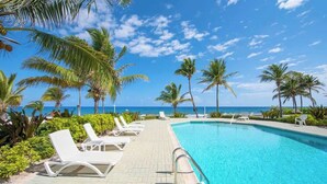 A poolside area with lounge chairs, palm trees, and a view of the ocean.