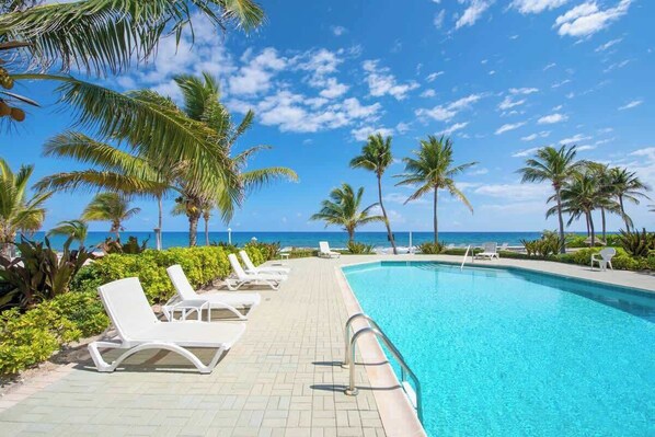 A poolside area with lounge chairs, palm trees, and a view of the ocean.