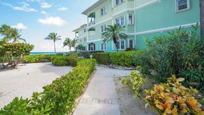 A multi-story hotel with a green facade, a paved walkway, and palm trees.