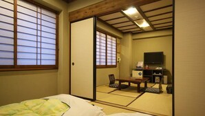 A traditional Japanese room with tatami flooring, a futon bed, a sliding door, and a television. - Shimizu City Hotel (Shizuoka)