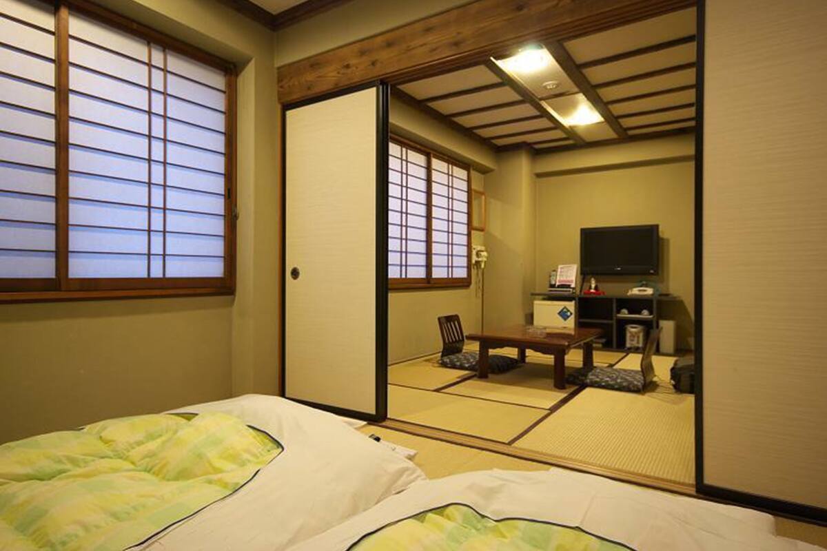 A traditional Japanese room with tatami flooring, a futon bed, a sliding door, and a television.