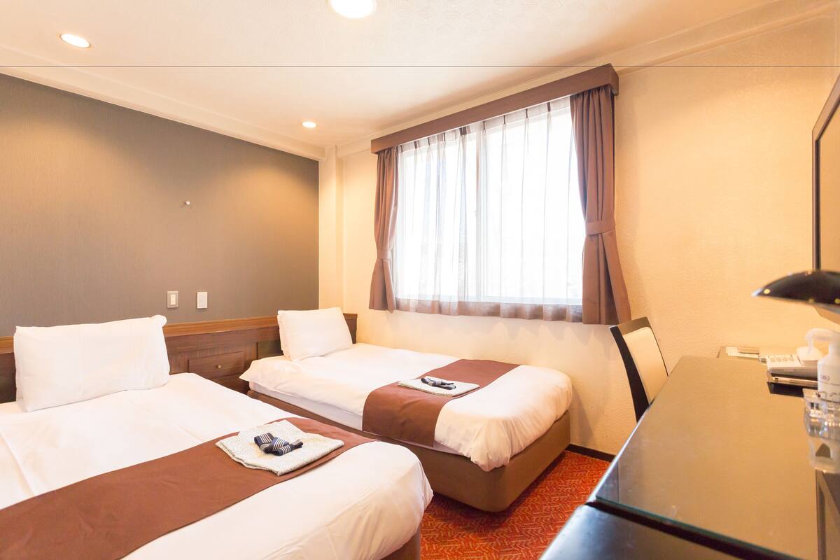 A hotel room with two beds, a desk, and a window with curtains.
