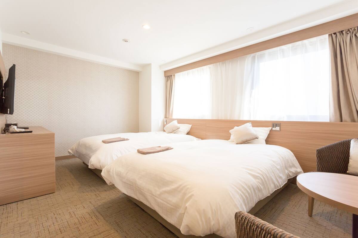 A hotel room with a large bed, a bedside table, a TV, and a window with curtains.