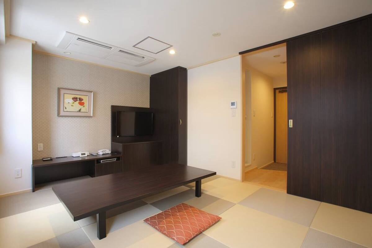 A modern room with a dark wooden bed, a flat-screen TV, a small desk, and a tatami mat.