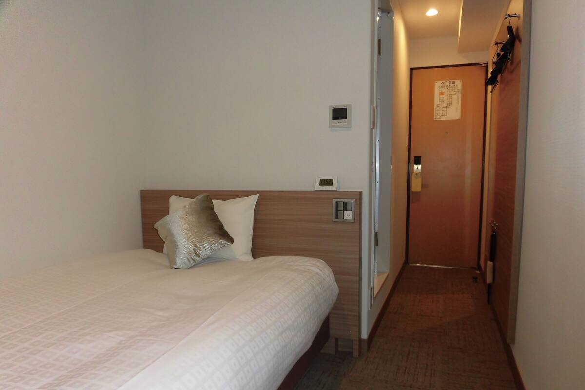 A hotel room with a bed, a wooden headboard, a nightstand, a wall clock, and a door with a sign.