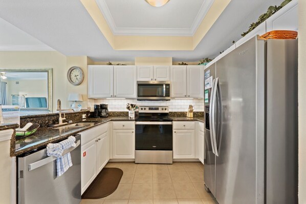 A modern kitchen with white cabinets, stainless steel appliances, and a clock on the wall.