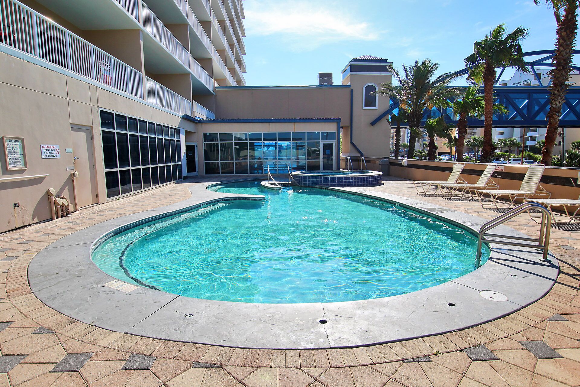 A hotel pool area with a clear pool, lounge chairs, and a building with balconies.