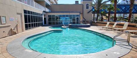 A hotel pool area with a clear pool, lounge chairs, and a building with balconies.