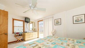 A bedroom with a bed, a ceiling fan, a dresser, a television, and a window with blinds. - Too Close - KDH MP 6, Ocean Views, 65 Yards to Beach, Foosball, 2 Kitchens, Flex Stays (Kill Devil Hills)