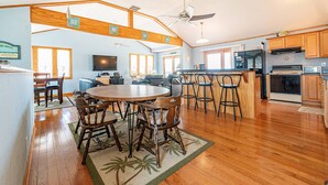 A spacious kitchen with wooden cabinets, a central island, and a dining area with a round table and chairs. - Too Close - KDH MP 6, Ocean Views, 65 Yards to Beach, Foosball, 2 Kitchens, Flex Stays (Kill Devil Hills)