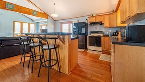 A modern kitchen with wooden cabinets, a central island with stools, a refrigerator, oven, and microwave. - Too Close - KDH MP 6, Ocean Views, 65 Yards to Beach, Foosball, 2 Kitchens, Flex Stays (Kill Devil Hills)