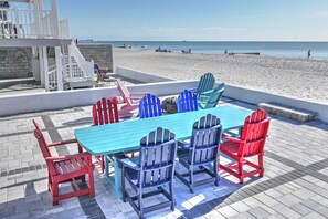 Un patio junto a la playa con una mesa azul y sillas Adirondack rojas y azules.