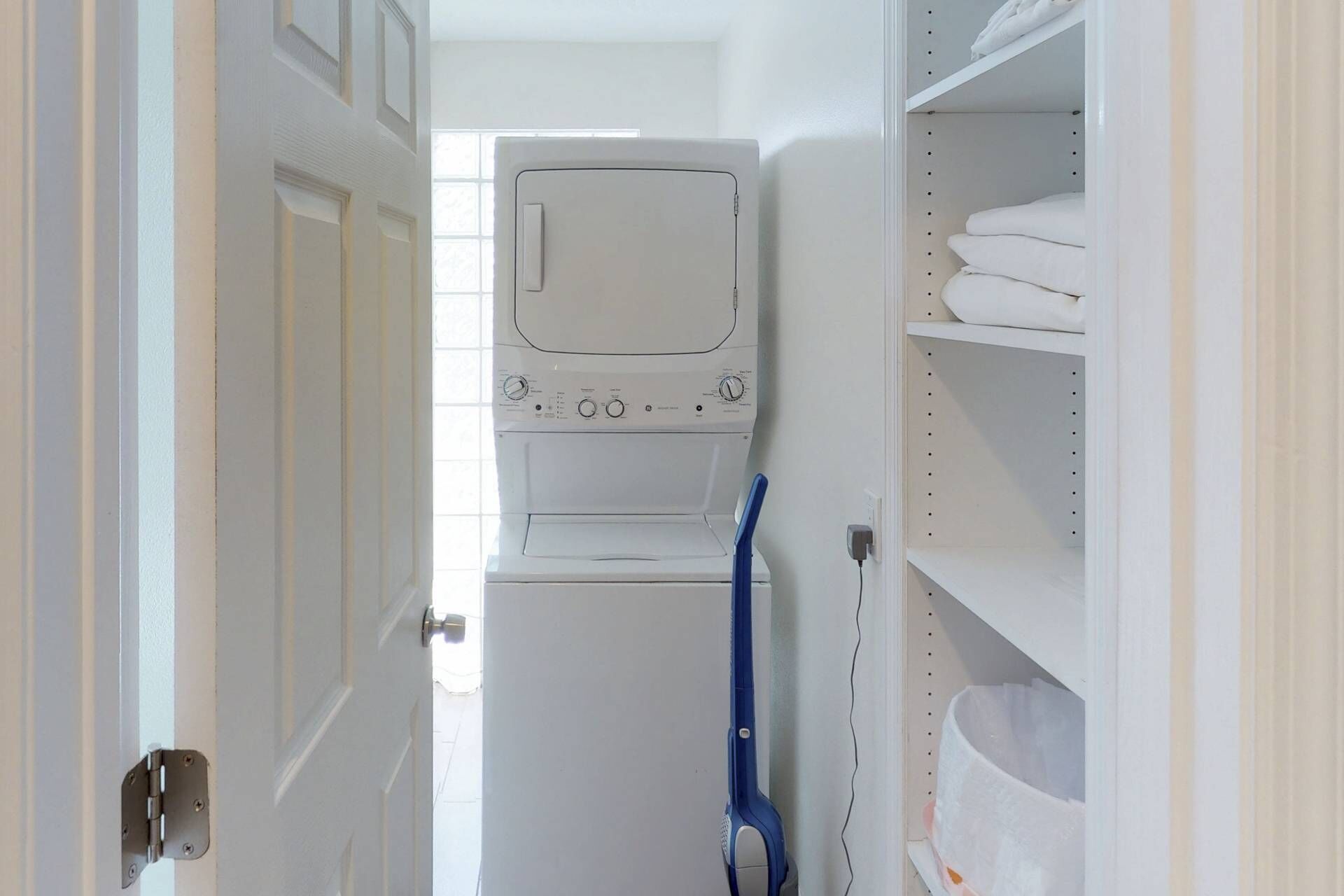 A laundry room with a washing machine and dryer, a blue mop, and shelves with folded towels.