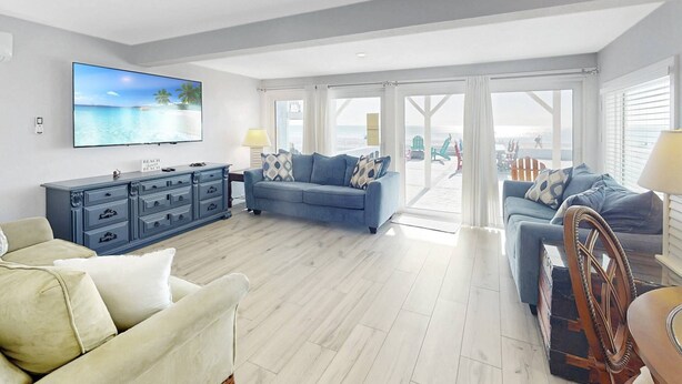 Un salón amplio con un televisor grande, un sofá azul, un sillón color beige y una silla de madera.