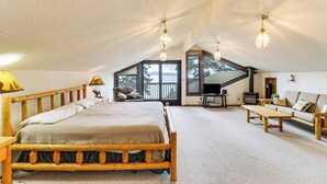 Ruime zolderkamer met een groot bed, houten meubels en een open haard.