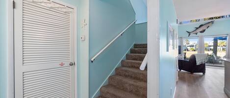 A staircase with a handrail, a closed door with a fire alarm, and a view of a room with a bed and a window.