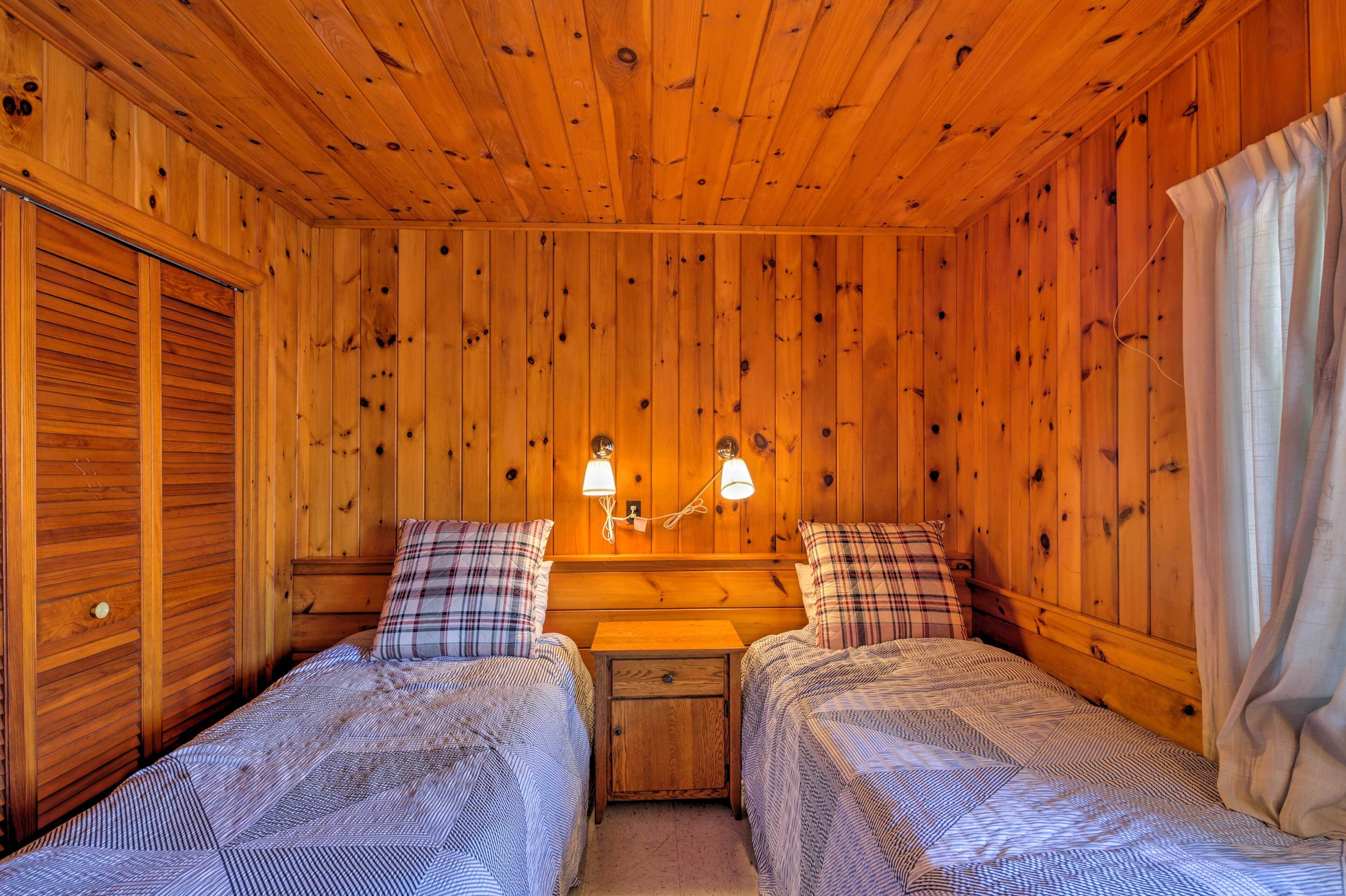 Quarto de cabana de madeira com duas camas, uma mesa de cabeceira e duas luminárias.