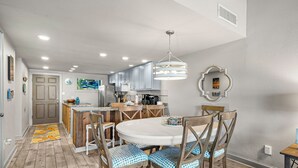 A modern kitchen with wooden cabinets, a white dining table, and blue cushioned chairs. - Unit 37, Sea Haven, 2 Bedroom Beach Condo (Panama City Beach)