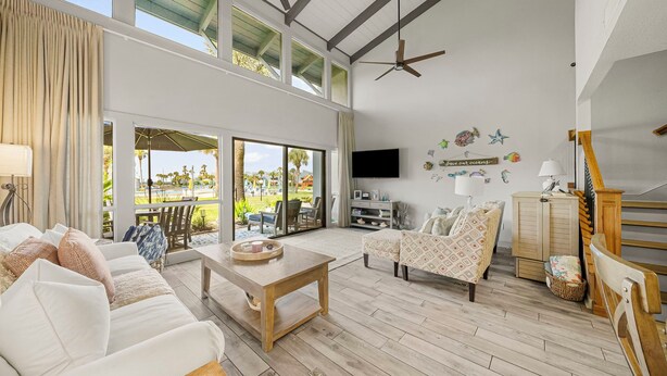 A spacious living room with a large window, a ceiling fan, and a flat-screen TV mounted on the wall. - Unit 37, Sea Haven, 2 Bedroom Beach Condo (Panama City Beach)