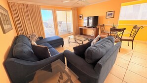 Un salon comprenant un ensemble de canapés, un téléviseur, un ventilateur de plafond et une vue à travers la porte vitrée.