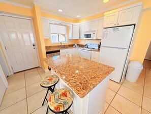 A kitchen with white cabinets, a granite countertop, a refrigerator, and two bar stools.