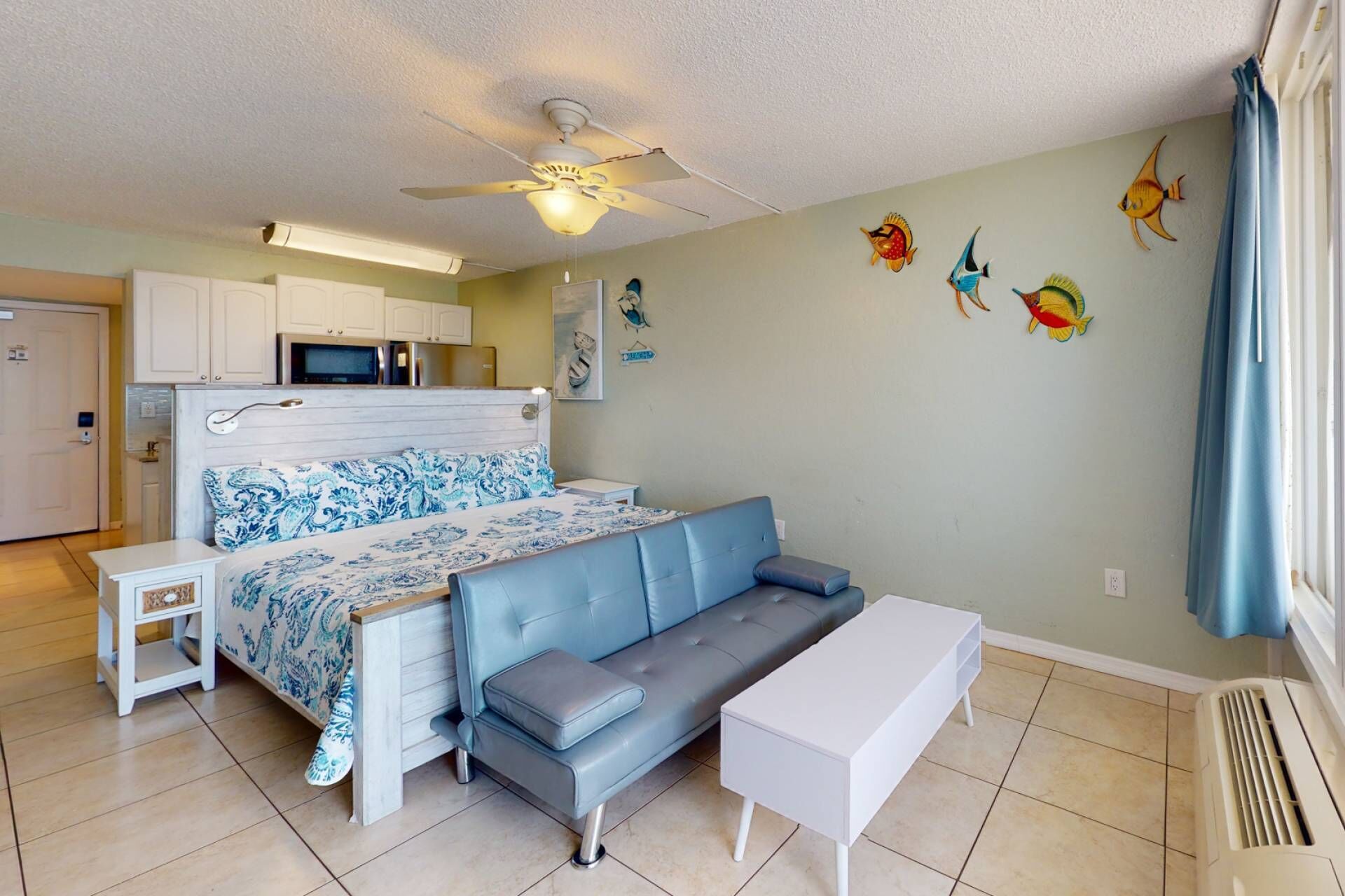 A compact bedroom with a bed, a sofa, a small table, and a ceiling fan.