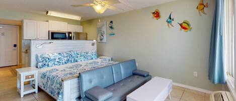 A compact bedroom with a bed, a sofa, a small table, and a ceiling fan.