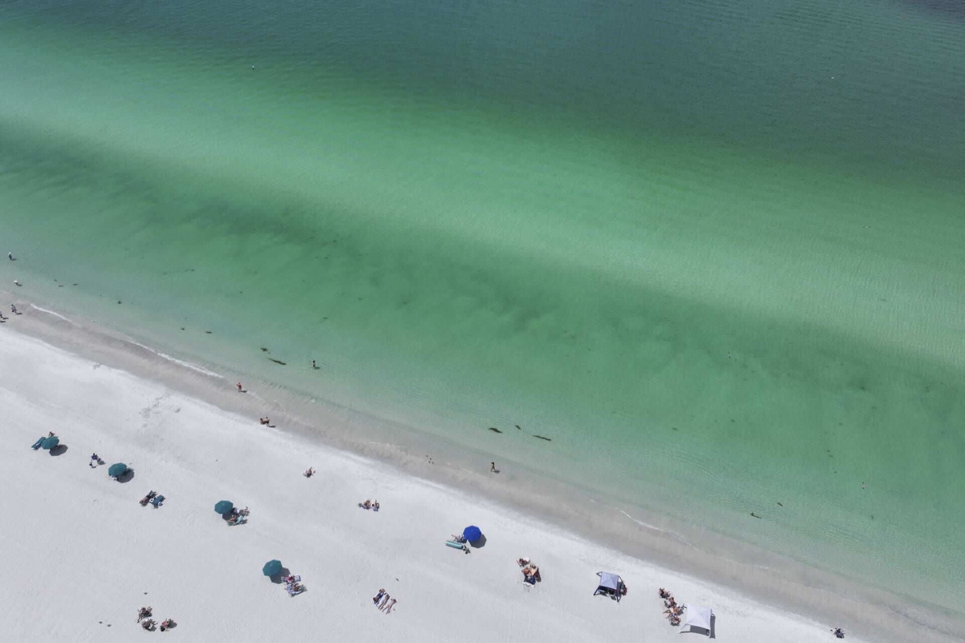 An aerial view of a beach with clear water, a sandy shore, and several beach umbrellas.
