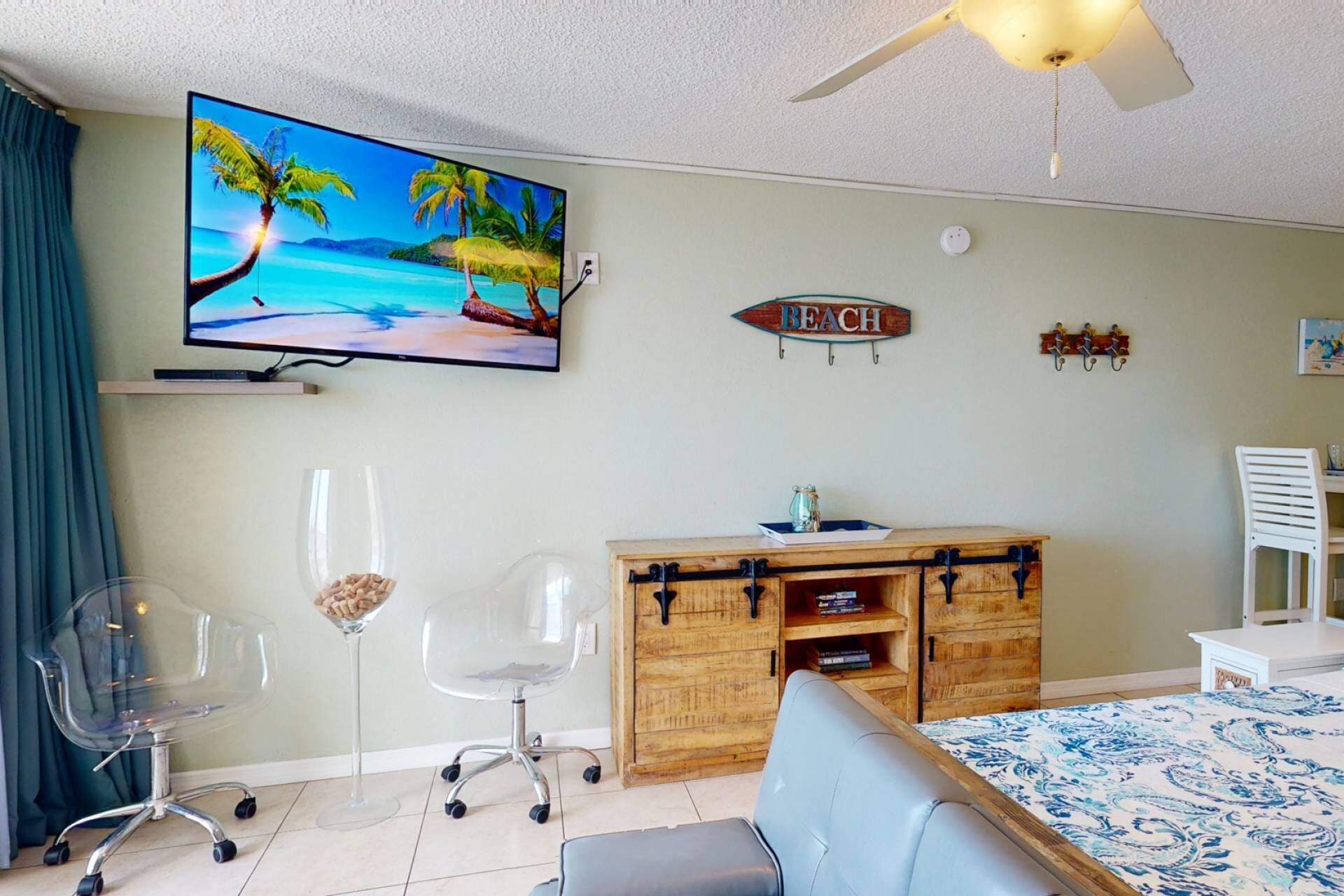 A room with a TV displaying a beach scene, a wooden cabinet, a blue sofa, and a ceiling fan.