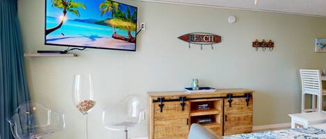A room with a TV displaying a beach scene, a wooden cabinet, a blue sofa, and a ceiling fan.