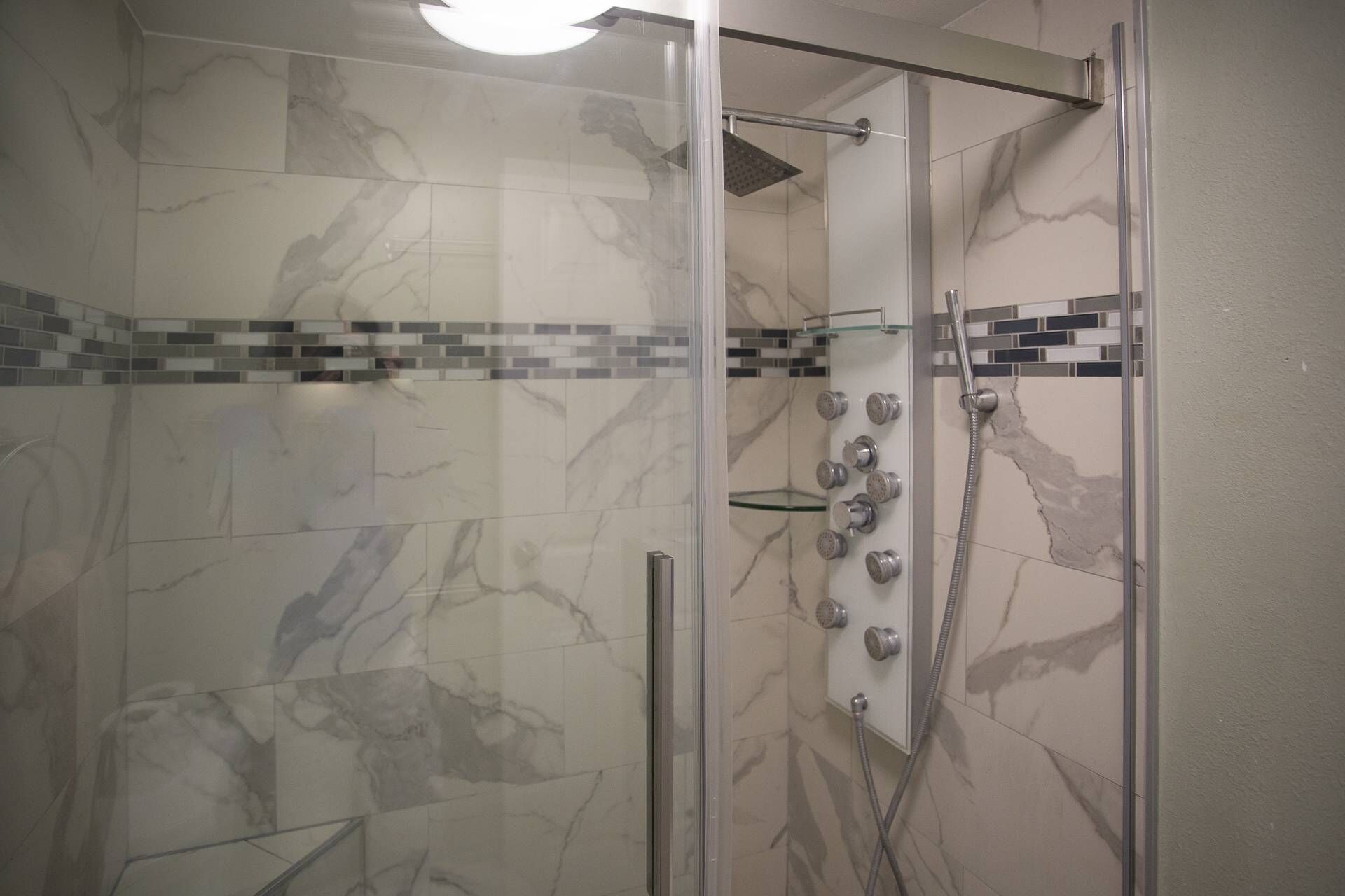 Een douche met glazen wanden, een betegelde vloer en wanden, een handdouche en een kraan op de muur.