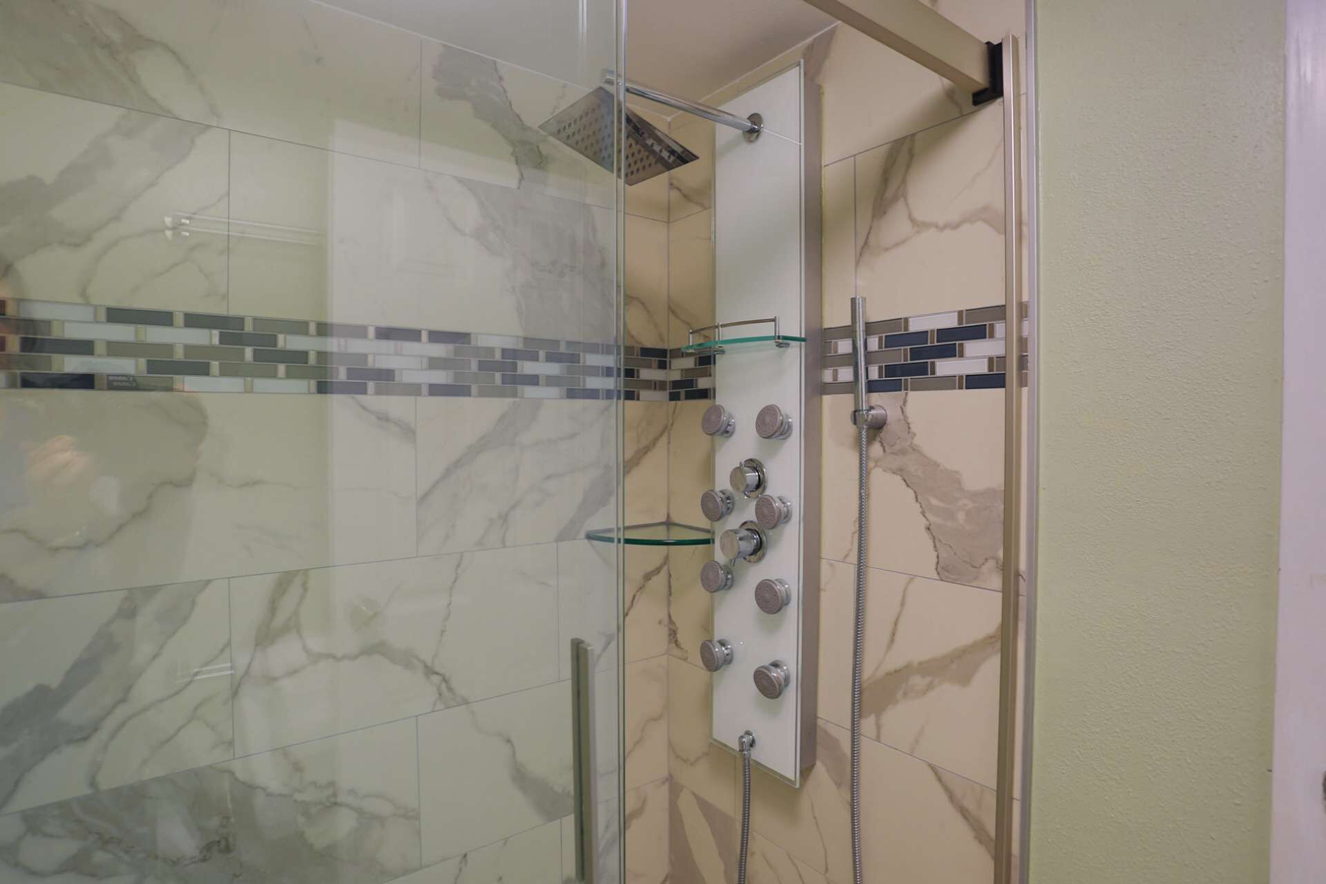 Une douche fermée par des parois de verre, avec un mur recouvert de carreaux de marbre, un pommeau de douche et un flexible de douche.