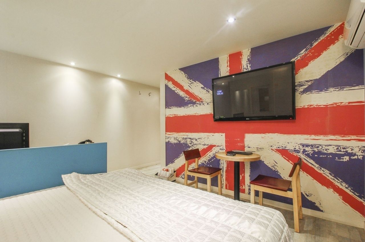 A hotel room with a bed, a television mounted on the wall, and a small table with two chairs.