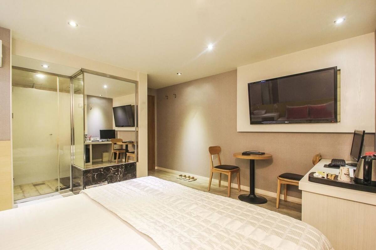 Una habitación de hotel con cama, escritorio, silla, televisor y espejo.