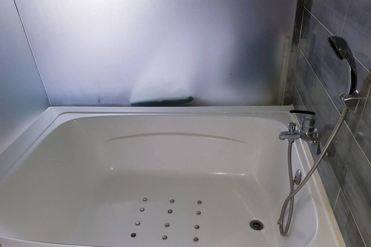 Una bañera blanca con cabezal de ducha manual y grifo integrado.