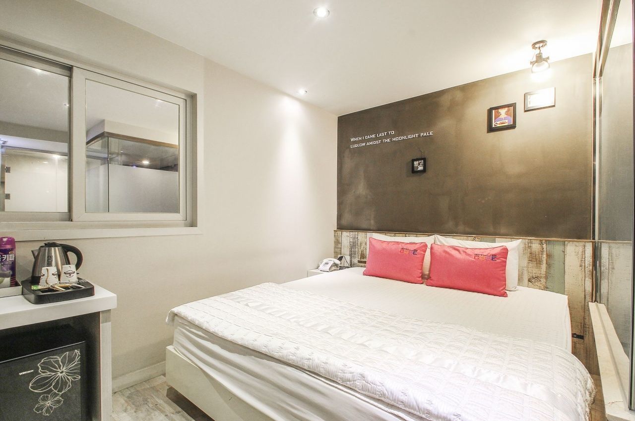 Habitación de hotel con una cama grande, una mesita de noche con hervidor, un espejo y una pared con una cita enmarcada.