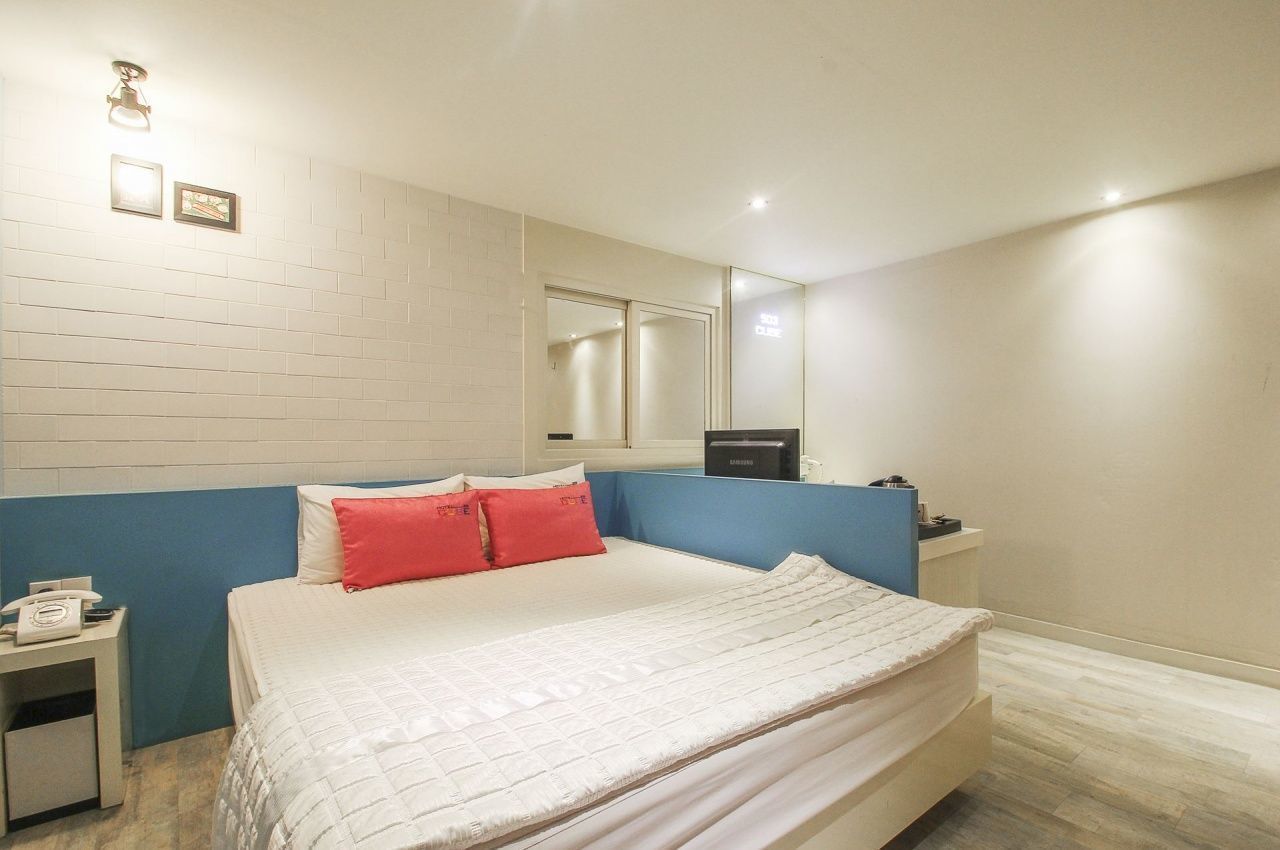 Un dormitorio con cama, mesita de noche, espejo y lámpara de pared.