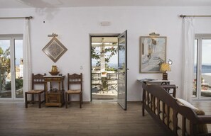 Una habitación con suelo de madera, un banco, una mesa con sillas, una puerta que da a un área exterior y un cuadro en la pared.