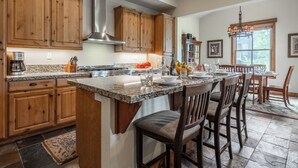 A kitchen with wooden cabinets, a stainless steel range hood, granite countertops, and a dining area with wooden chairs and a table. - Lodges 1140 | Shuttle | Shared Hot Tub (Mammoth Lakes)